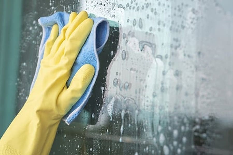 Gloved hand wiping condensation from an interior window in a humid Florida home
